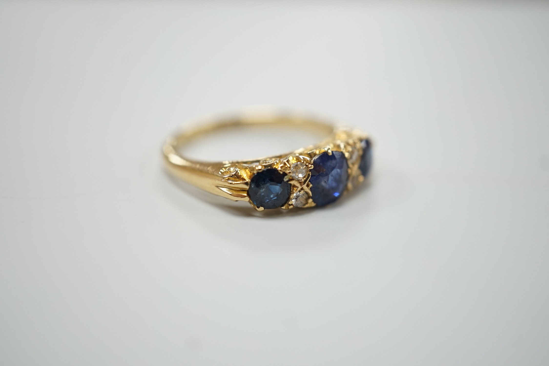 A George V 18ct gold and three stone sapphire set half hoop ring, with four diamond chip spacers, size M, gross weight 4.4 grams.